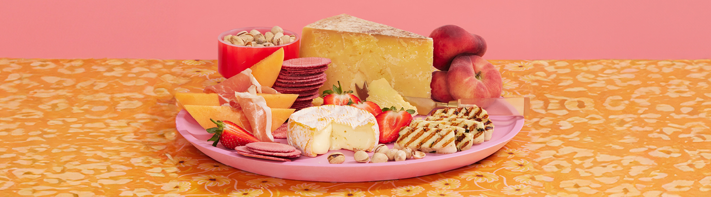 A cheeseboard with pears, strawberries and almonds sits on a orange tablecloth.