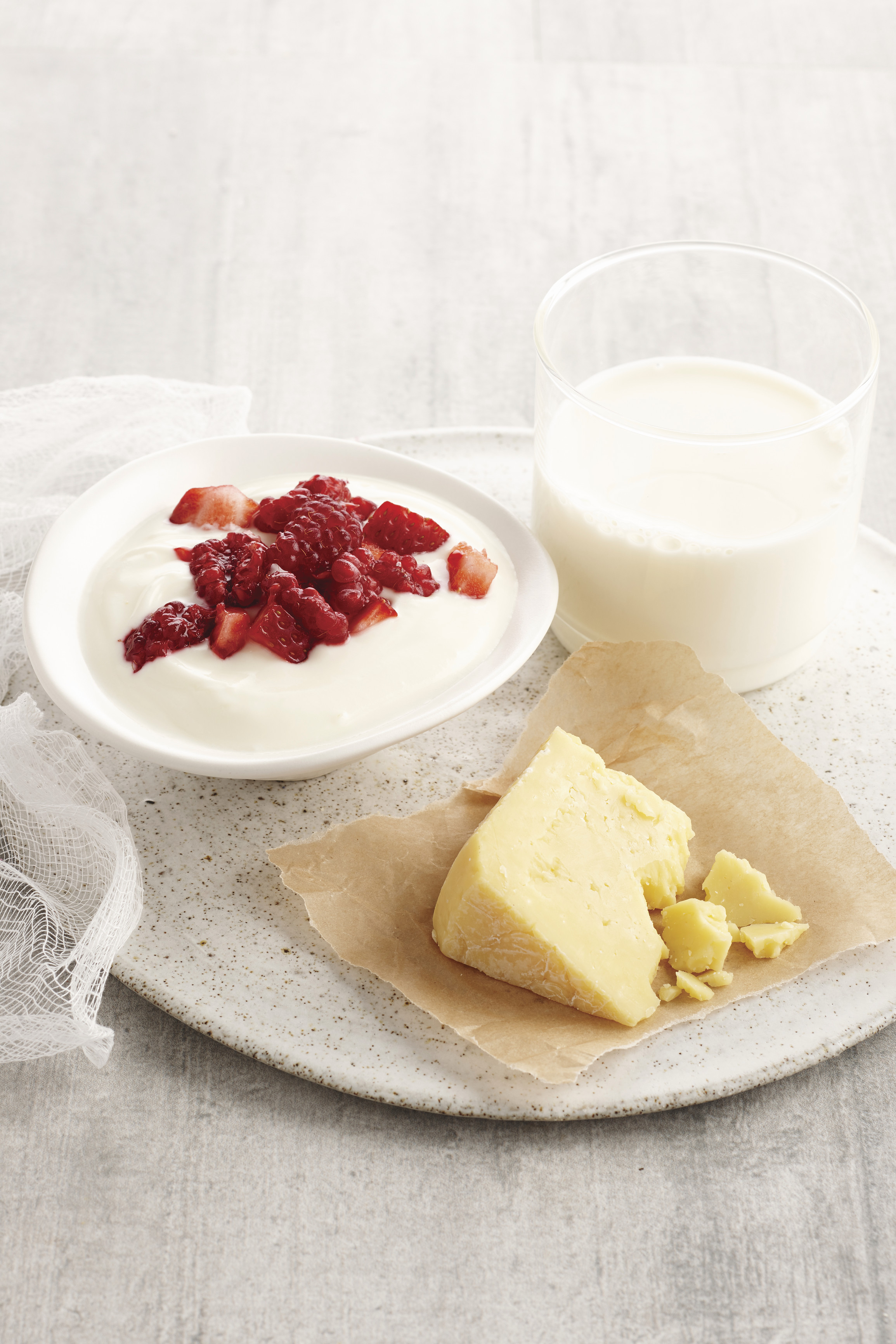 Wedge of cheese, glass of milk and bowl of yoghurt and berries