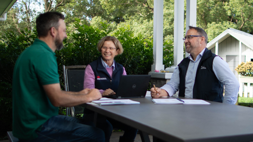A Dairy Australia team member is meeting with two farmers in their outdoor patio.