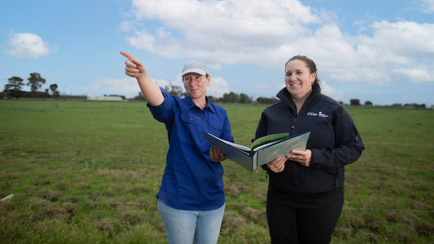 Two women holding a folder standing in pasture, one is pointing in the distance