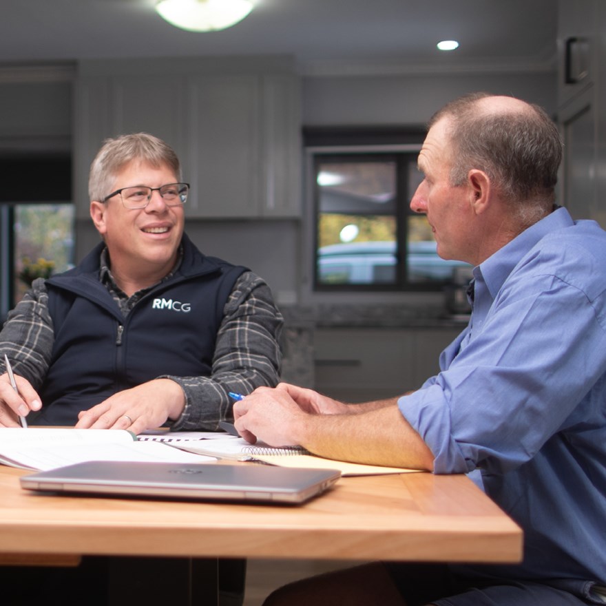 Two farmers are speaking about their farm business at a dinning table.