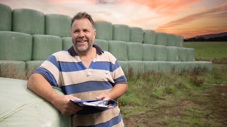 Man standing in front of silage bales holding folder. Sunset in the distance.