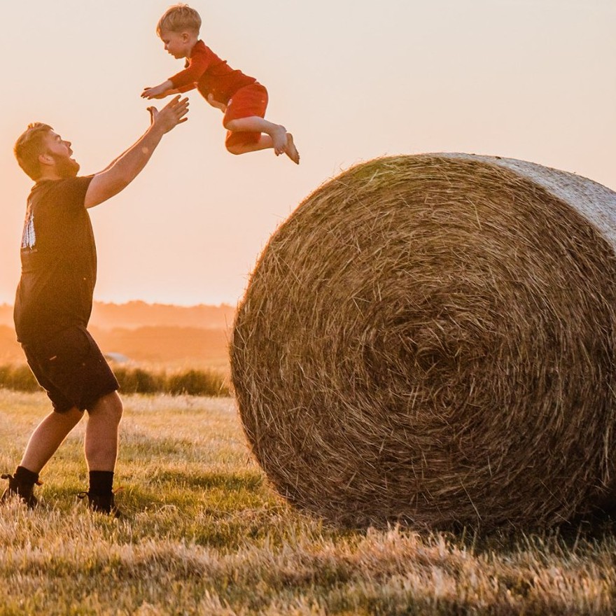 Man playing with young child on hay bale